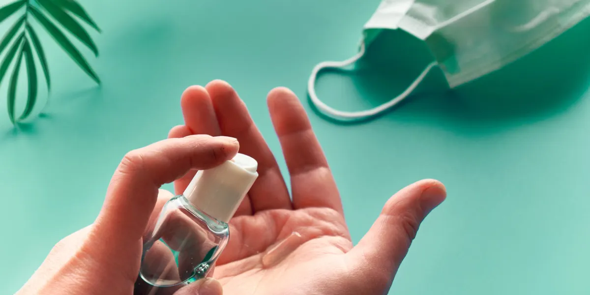 hands of senior female with sanitizer, hand soap mint green background with face mask and palm tree leaf social isolation, hygiene, prophylactic measures to fight novel coronavirus causing covid-19