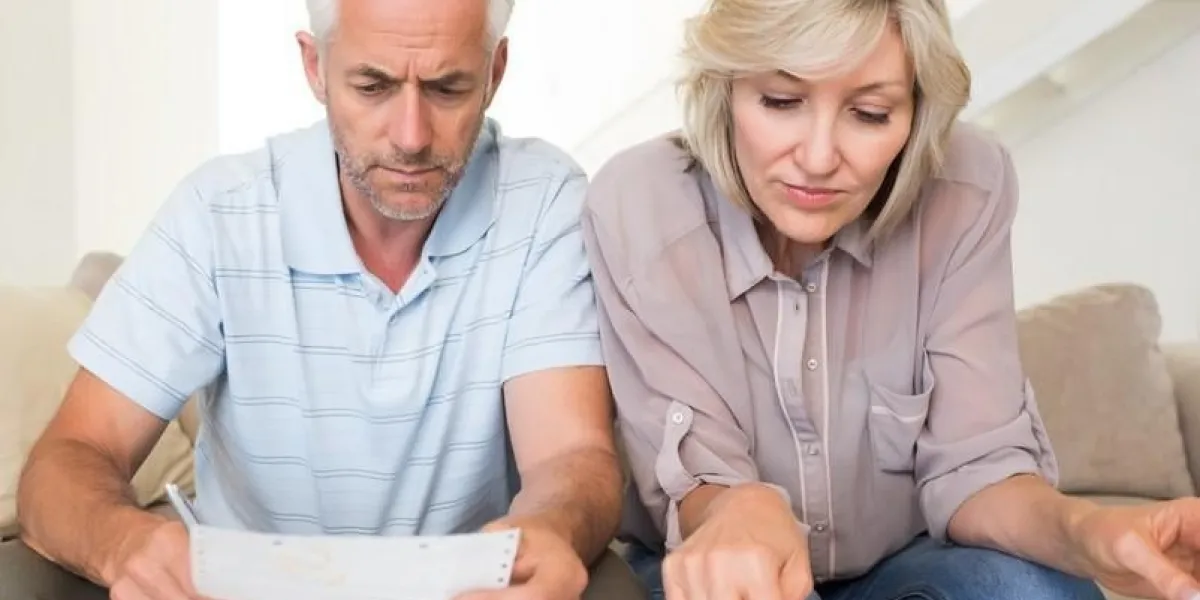 homme mûr concentré et femme avec factures et calculatrice assis sur le canapé à la maison