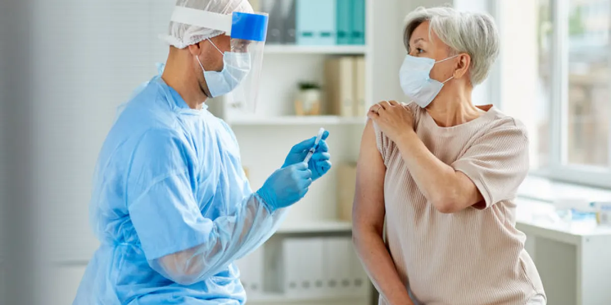 side view shot of male nurse wearing protective mask and gloves preparing medical syringe for giving injection to senior patient