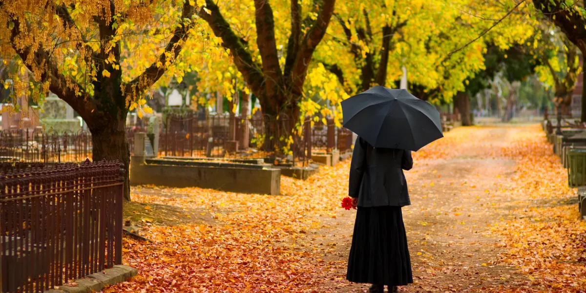 mourning woman wearing black in cemetery in fall