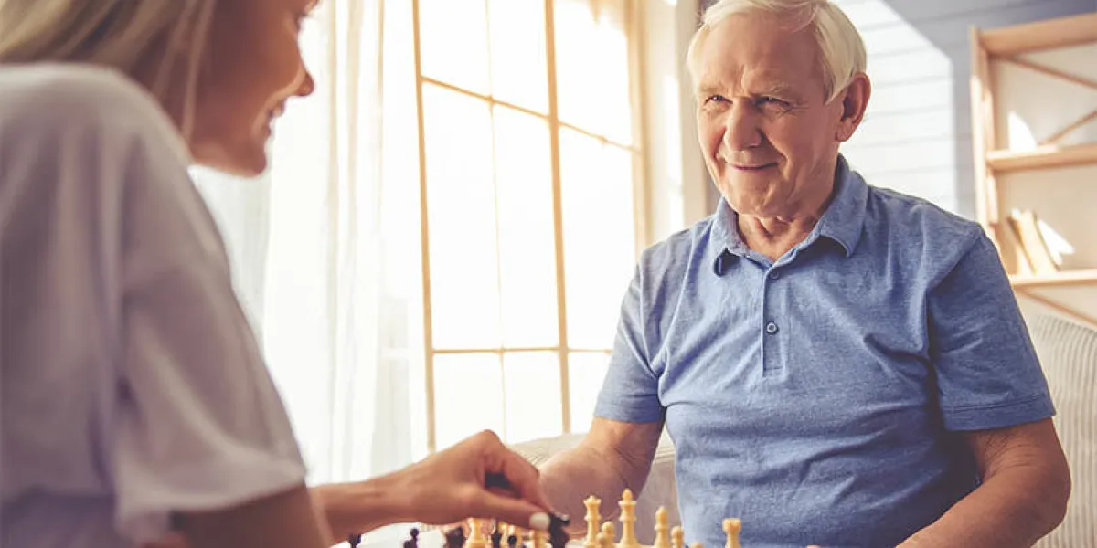 beautiful young girl-volunteer and handsome old man are playing chess and smiling