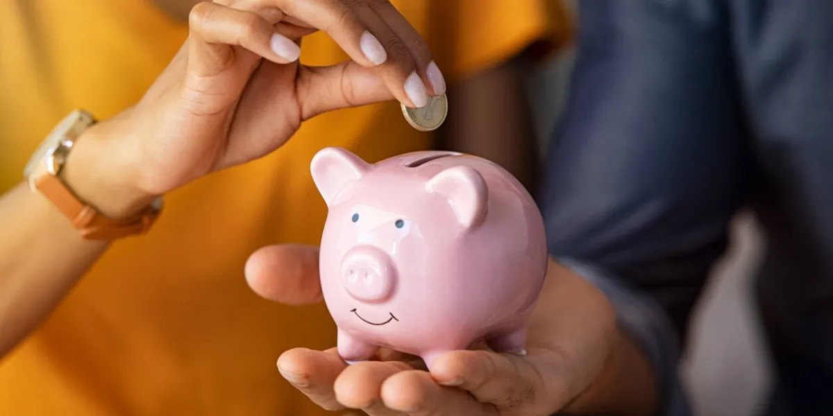 close up of man holding pink piggybank while woman putting coin in it indian young couple saving money for their wedding close up of woman hand putting euro money in piggy bank to save for the purchase of an house