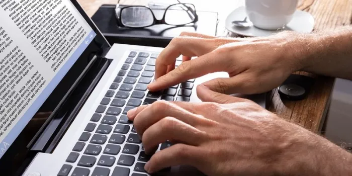 person's hand typing on laptop over wooden desk