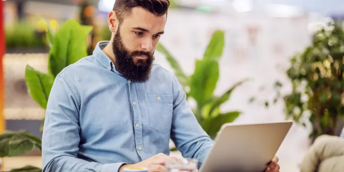 young handsome busy entrepreneur sitting in cafeteria and using laptop for work