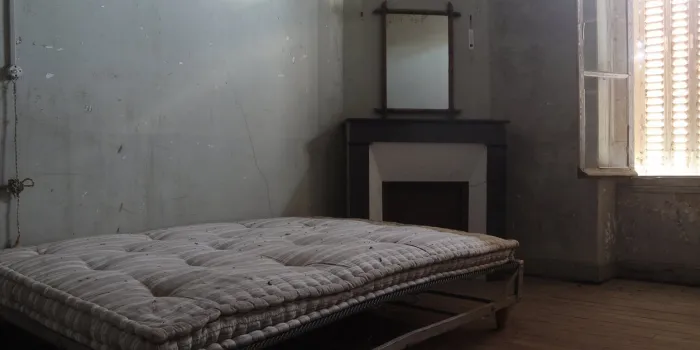 in an abandoned room of an old house, an old mattress on a metal bed facing the window