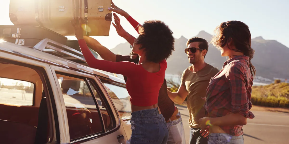 friends loading luggage onto car roof rack ready for road trip