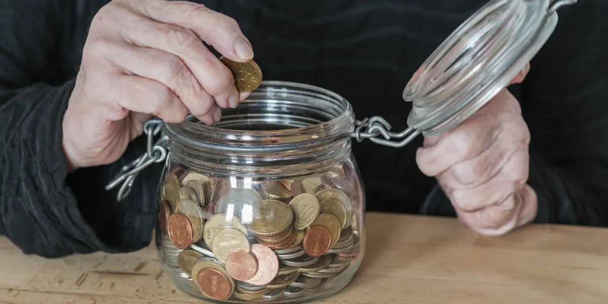 hands of an old woman holding a mason jar with coins