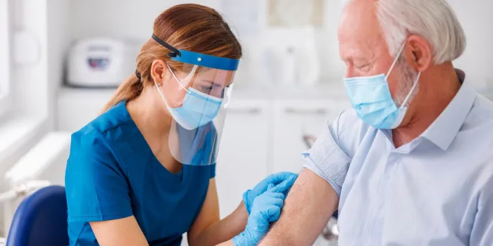 elderly man wearing protective medical face mask receiving covid 19 or seassonal flu vaccine at medical clinic, doctor or nurse touching and disinfecting the vaccine application spot
