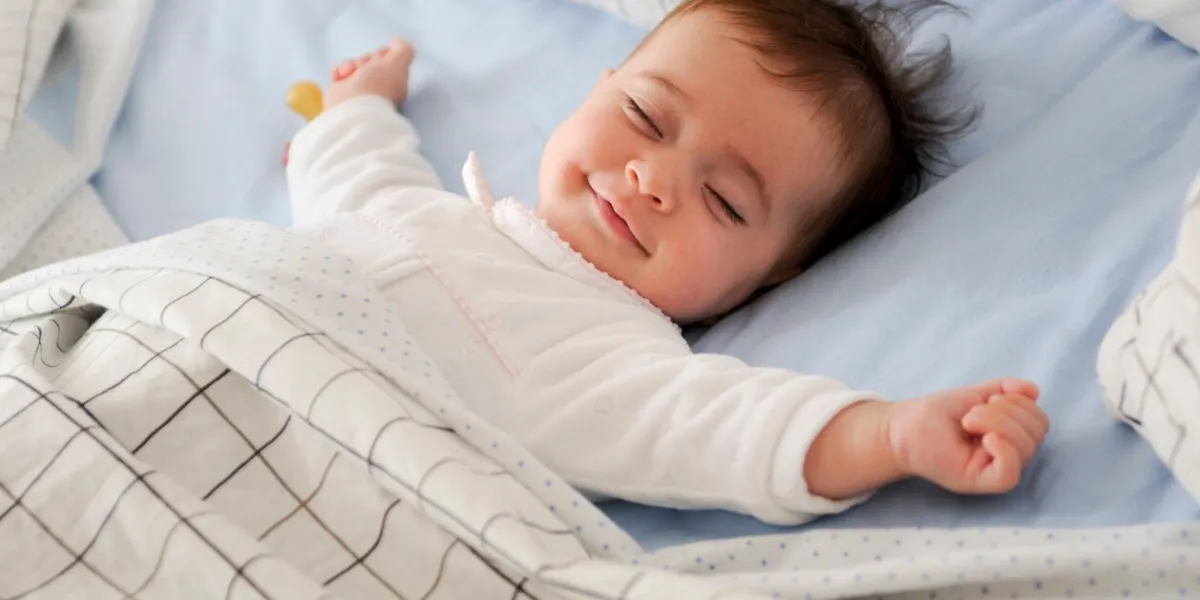 smiling baby girl lying on a bed sleeping and smiling on blue sheets