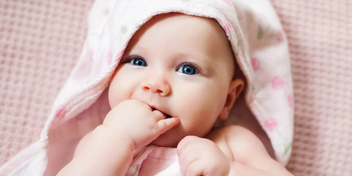 authentic portrait of 4 months baby girl wrapped in hooded towel after bath horizontal image in soft pink tones