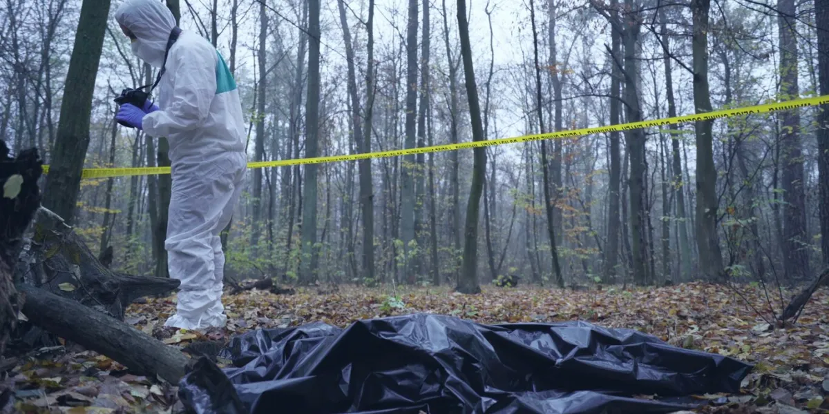 forensic expert photographs the crime scene, with the victim's body lying on the ground in a bag