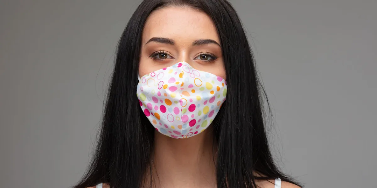 young woman in a colorful fabric face mask during the coronavirus pandemic in a head and shoulders portrait on grey conceptual of the fashion style