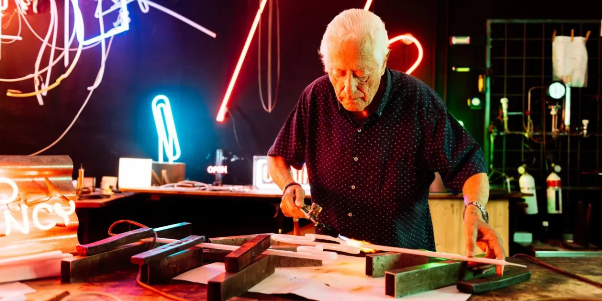 a master neon sign artisan carefully heats a glass tube in his shop, surrounded by vibrant neon signs and tools of the trade