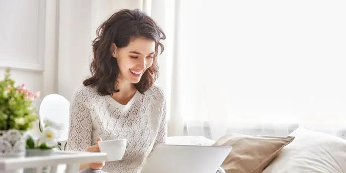 happy casual beautiful woman working on a laptop sitting on the bed in the house