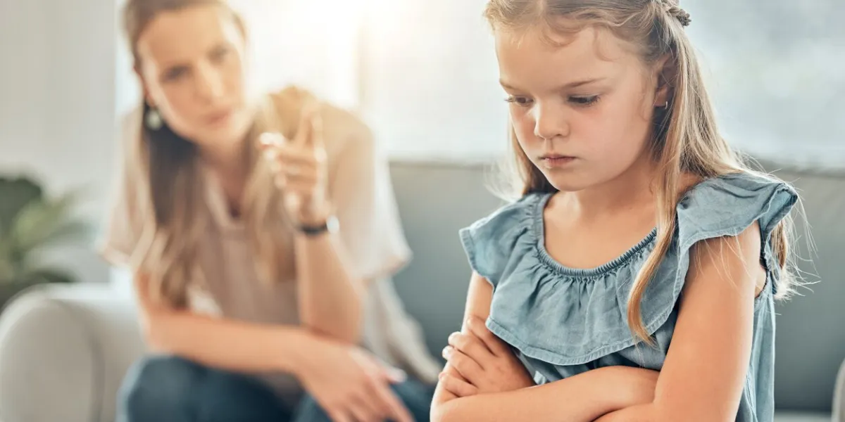 closeup of an adorable little girl standing with arms crossed and looking upset while being scolded and reprimanded by her angry and disappointed mother at home a woman punishing her young daughter
