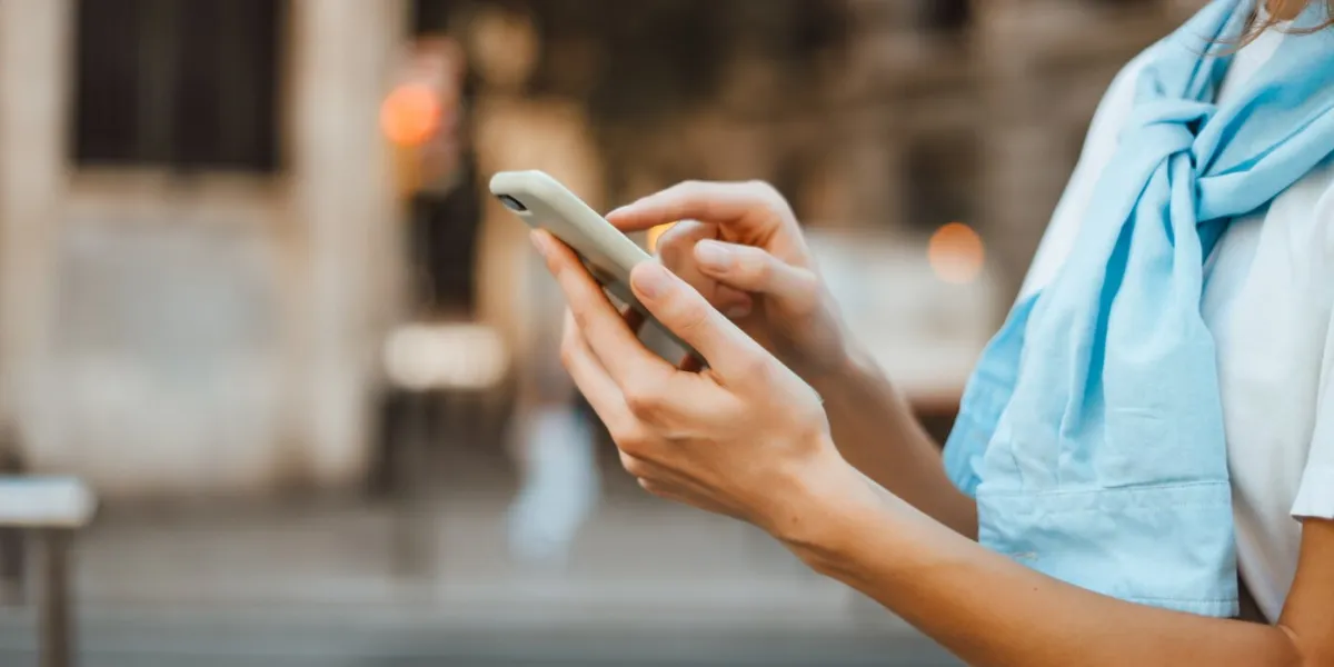 close-up photo of female hands with smartphone young woman typing on a mobile phone on a sunny street