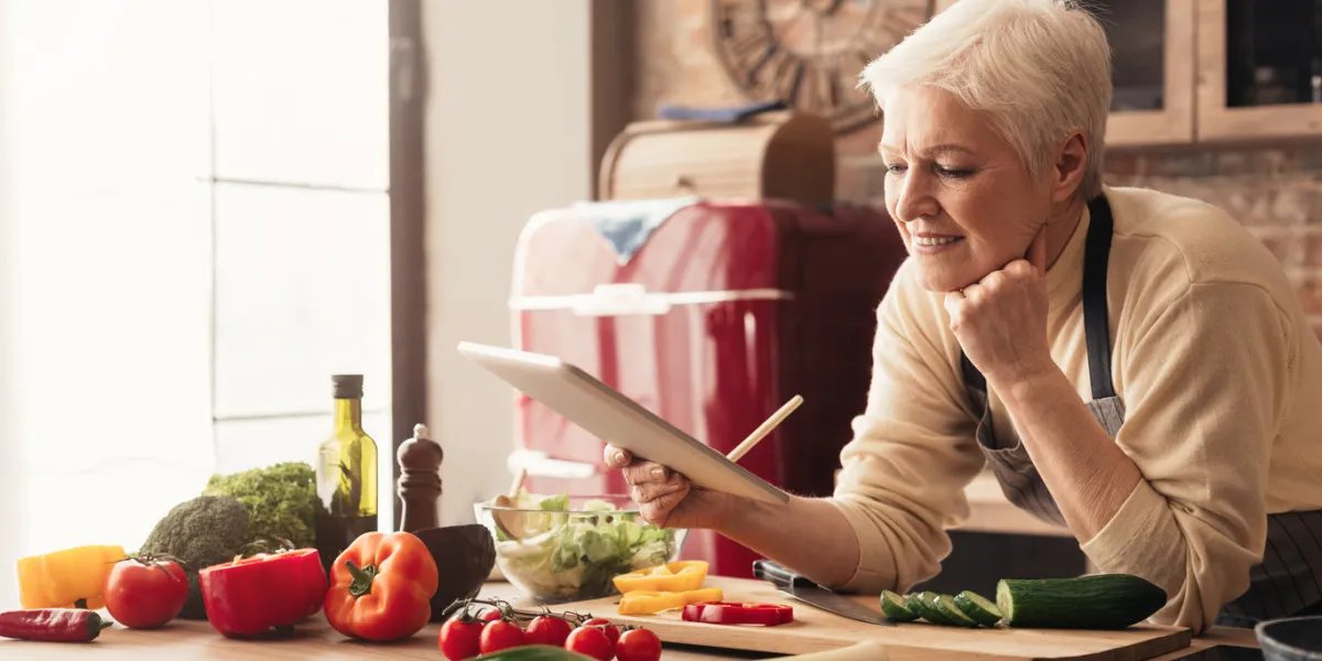 dreamy senior housewife ordering food online, browsing on digital tablet at kitchen, panorama with free space