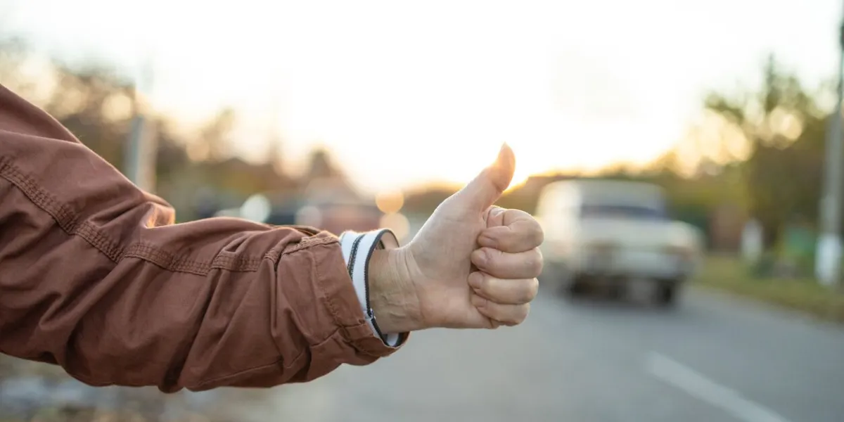 female hand and hitchhiking sign on road, traveling by autostop in the city woman try stop car thumb up adventure and tourism concept