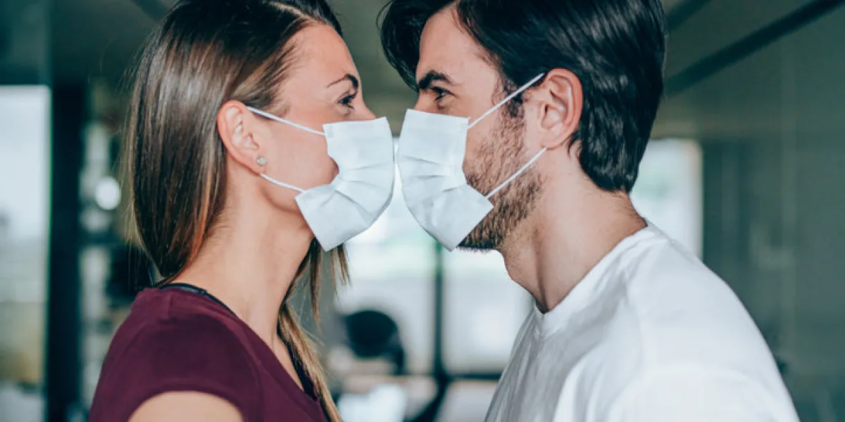 beautiful happy young couple wearing protective face masks and kissing each other side view of young man and young woman in medical masks kissing while they are in home isolation during coronavirus covid-19 quarantine