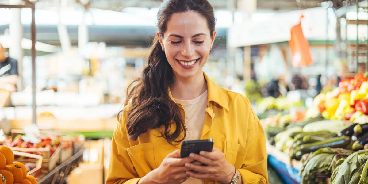 woman at the farmer's market shopping, sending a text message on her smart phone young cheerful woman at the market smiling girl decided to cook a delicious and healthy meal