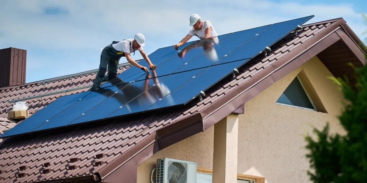 workers building photovoltaic solar panel system on rooftop of house men technicians in helmets installing solar module with help of hex key outdoors renewable energy generation concept