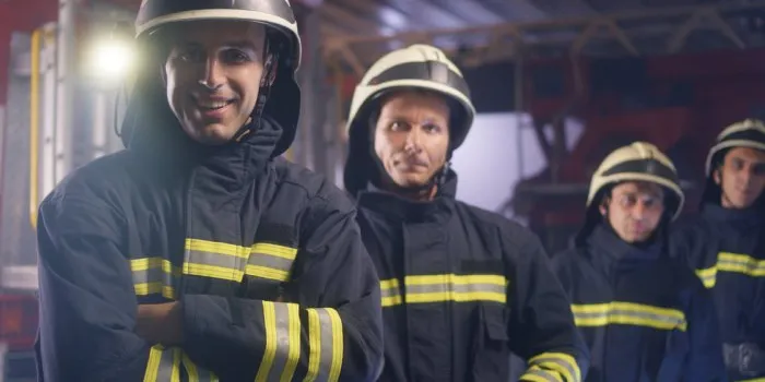 group of confident firemen putting on hardhats and looking at camera while working on fire station together