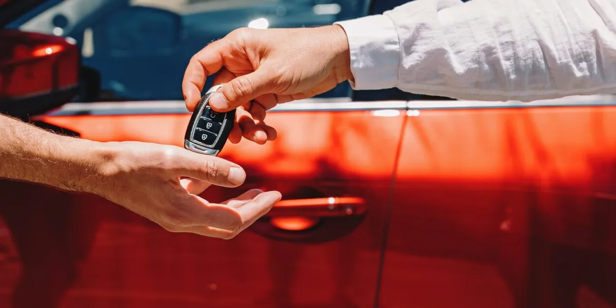 dealer giving car keys to the new owner close-up of hands on the background of red automobile