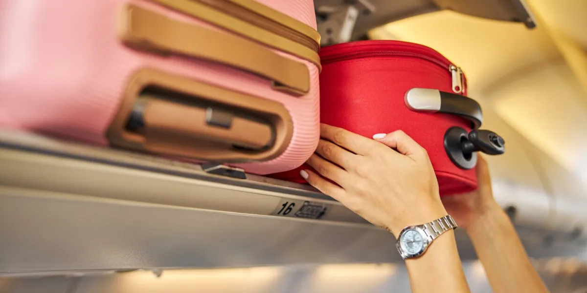 arms shoving a small piece of luggage to the top shelf of an aircraft