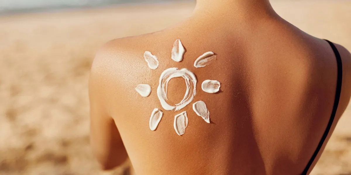 skin care sun protection woman apply sun cream woman with suntan lotion on beach in form of the sun portrait of female with drawn sun on a shoulder suncream girl holding moisturizing sunblock