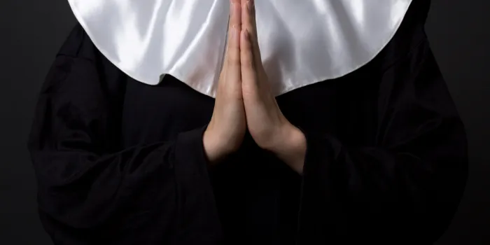religion concept - hands of woman nun praying over grey background