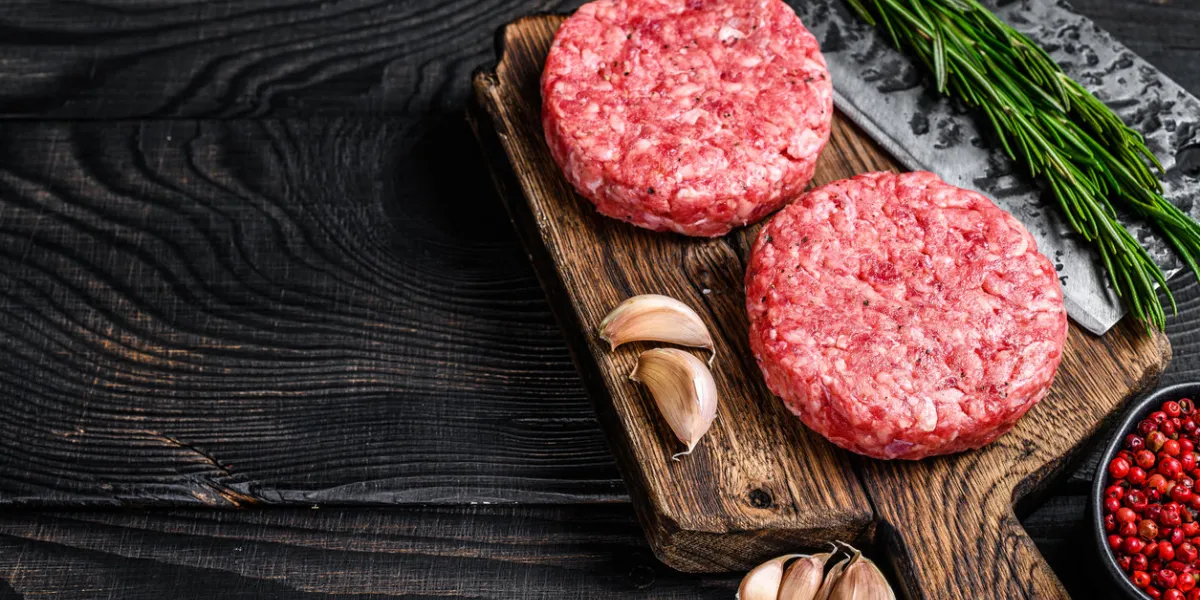 raw steak cutlets with mince beef meat and rosemary on a wooden cutting board with meat cleaver black wooden background top view copy space