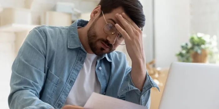 upset frustrated young man reading bad news in postal mail letter paper document sit at home table, depressed stressed guy worried about high bill tax invoice, overdue debt notification money problem
