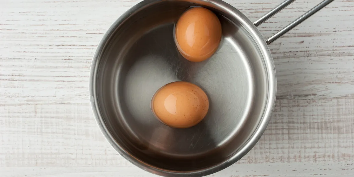 two eggs in the water in a metal pan on the table top view