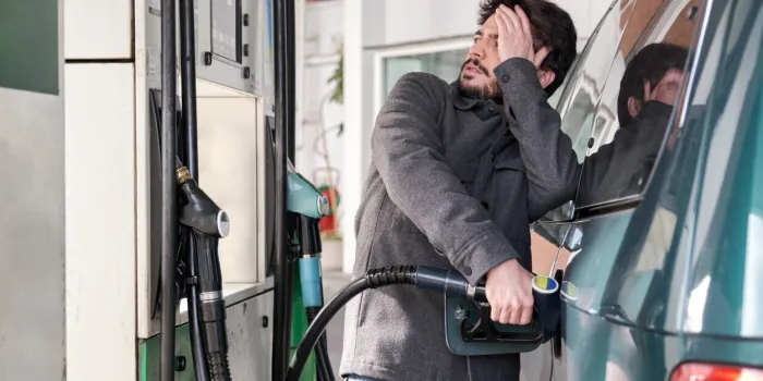 young man refueling his vehicle while looking worried at the high gas prices at a gas station