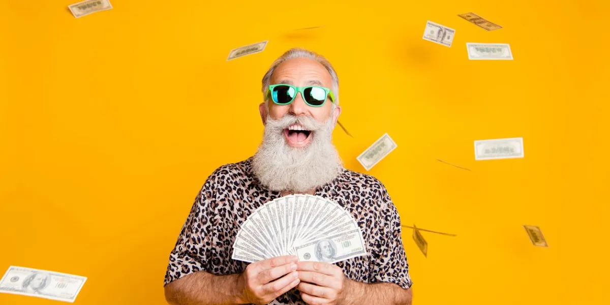 photo of elderly old confident rich man holding banknotes in his hands and being, rained with currency while isolated with yellow background