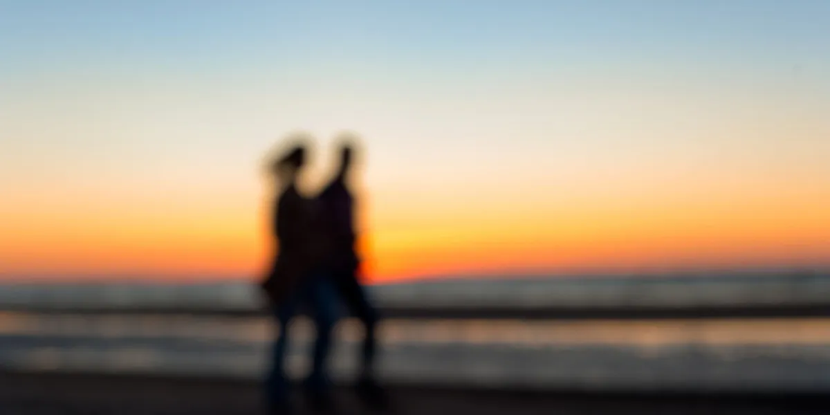 two people defocused silhouettes walking along the beach on multicolored sunset long exposure outdoors vibrant horizontal image