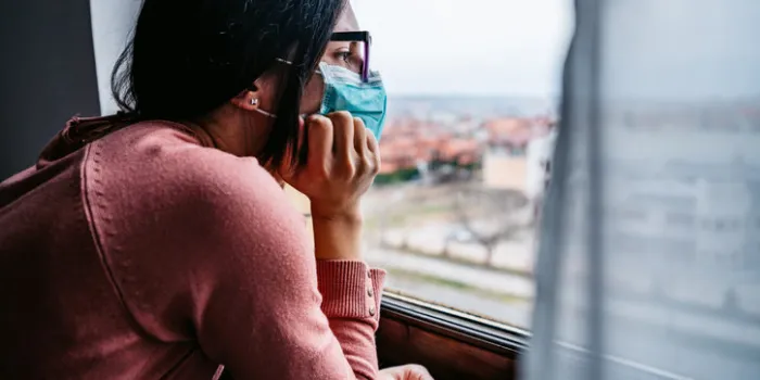 woman in quarantine wearing a mask and looking through the window pandemic of coronavirus   covid-19