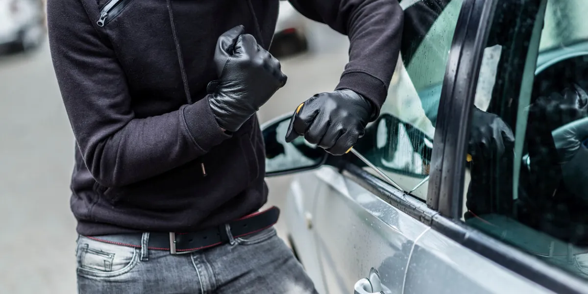 the man dressed in black with a balaclava on his head trying to break into the car he uses a screwdriver car thief, car theft concept