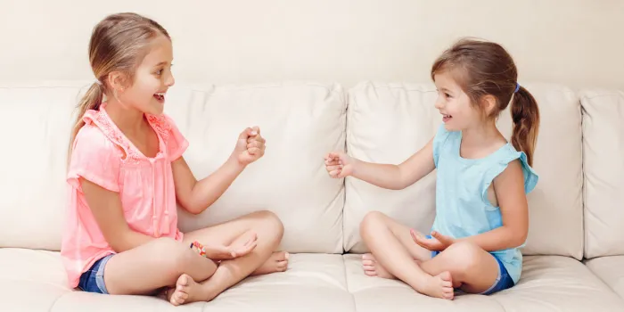 two girls friends playing rock paper scissors hand game caucasian children sitting on a couch playing together interesting entertaining activity for kids authentic candid lifestyle moment