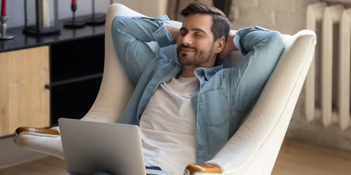 peaceful young man daydreaming in comfortable armchair with computer on knees calm guy taking break after working with laptop, controlling fatigue or stress, resting alone in living room at home