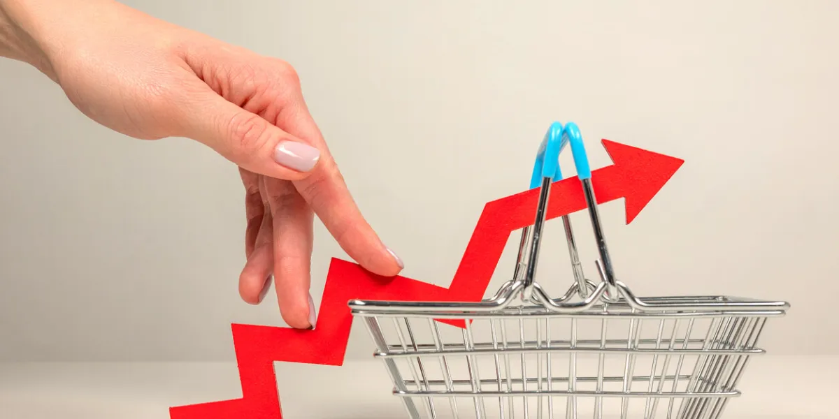 the fingers of a woman's hand step up the arrow of a chart lying on a shopping basket crisis and rising commodity prices concept