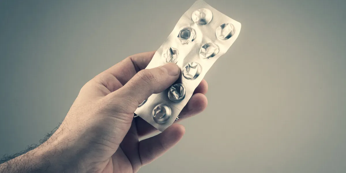 closeup of caucasian male hand holding empty pills blister silver packaging foil against grey background
