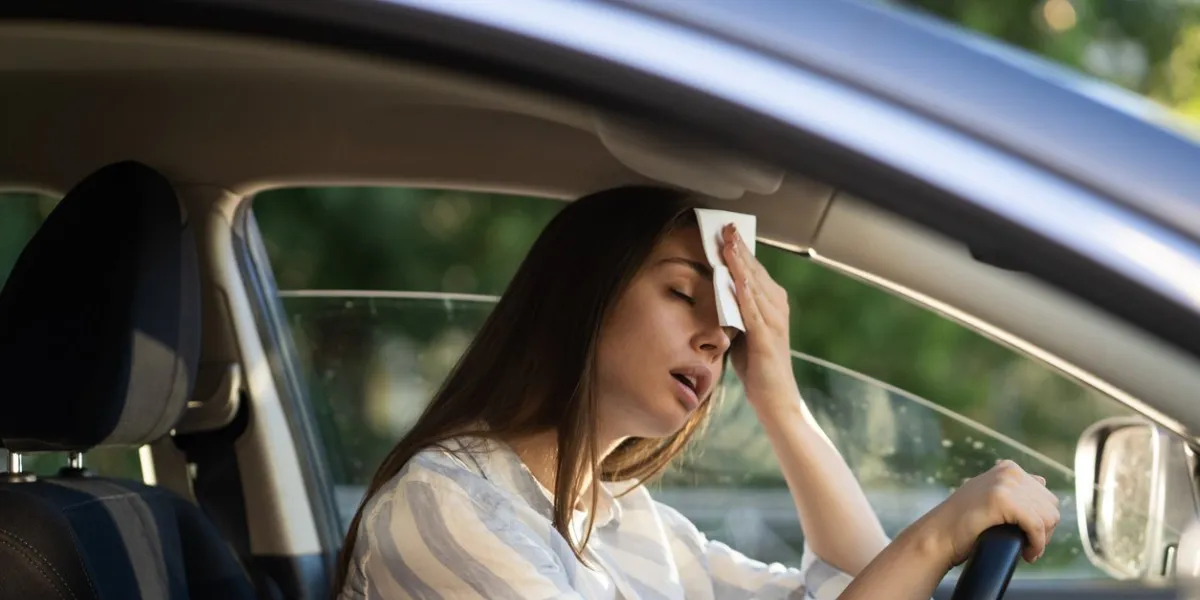 girl driver being hot during heat wave in car, suffering from hot weather, has problem with a non-working air conditioner, wipes sweat from her forehead with tissue summer, heat concept
