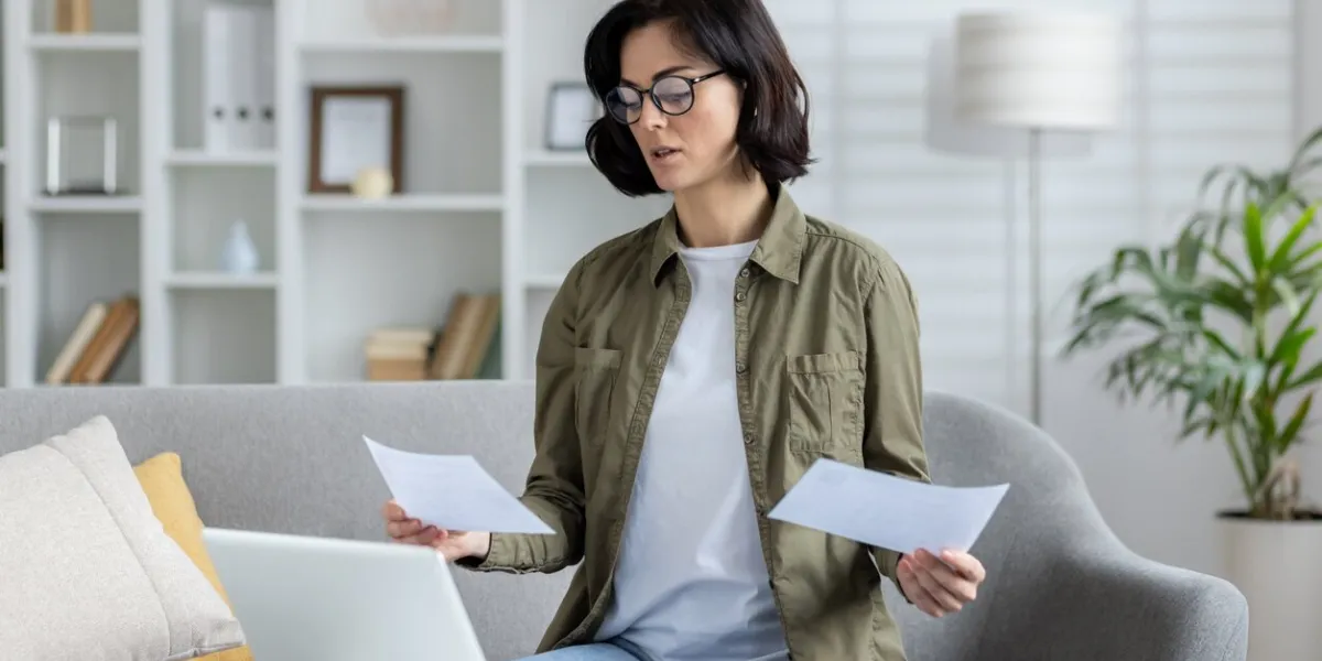 a young businesswoman works remotely from home, talks via video call with colleagues and clients, holds documents and bills in her hands