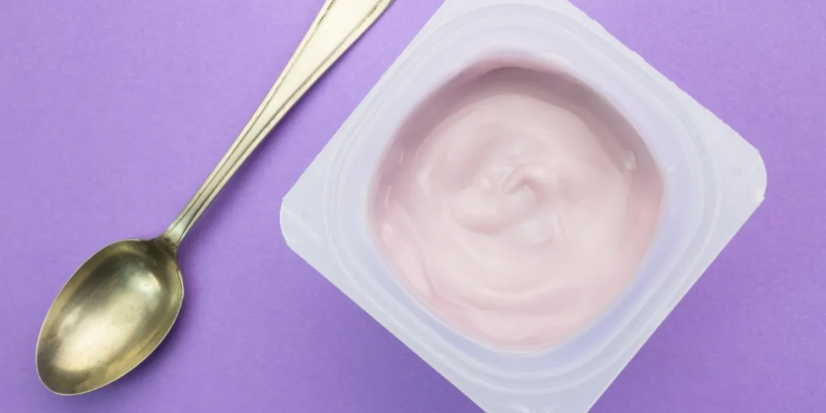 healthy strawberry fruit flavored yoghurt with natural coloring in plastic cup isolated on purple background with small silver spoon - top view