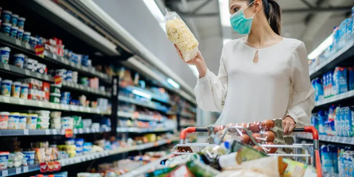 young person with protective face mask buying groceries supplies in the supermarketpreparation for a pandemic quarantine due to coronavirus covid-19 outbreakchoosing nonperishable food essentials