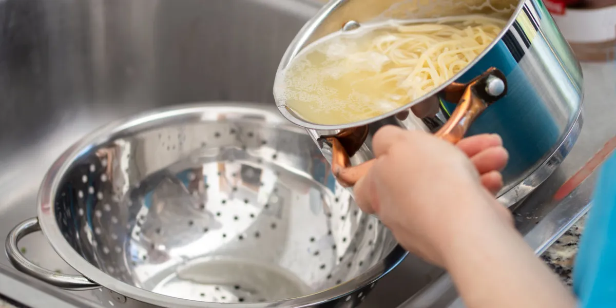 woman separating water from spaghetti withempty silver colander