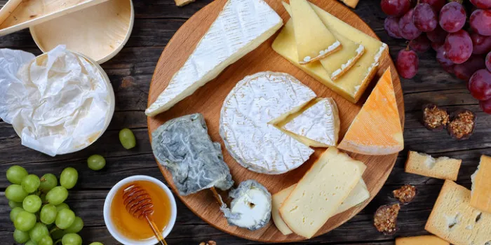 set of authentic french cheese plate served with grapes, honey, homemade chocolate sweets and nuts on wooden round tray on dark wooden background, view from above