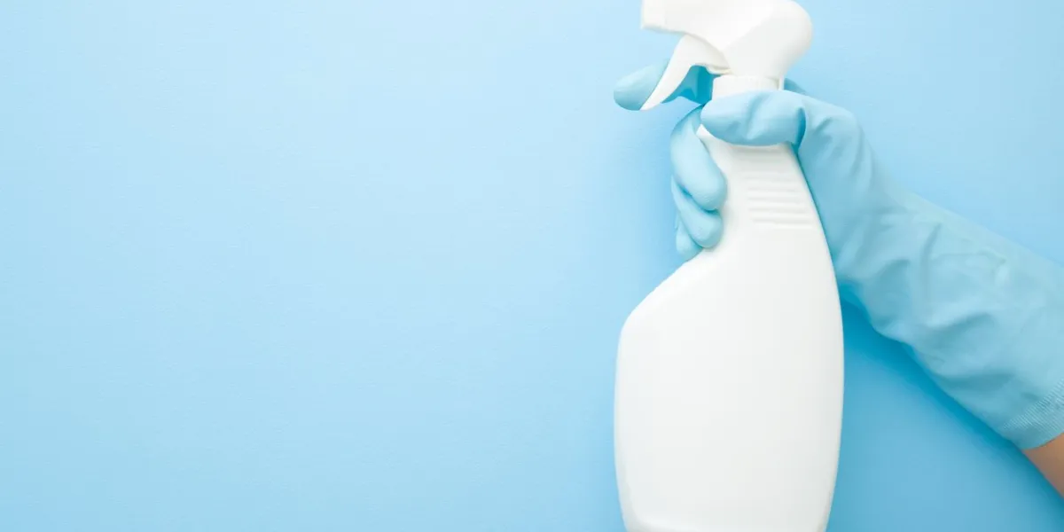 hand in rubber protective glove holding white spray bottle detergent for different surfaces in kitchen, bathroom and other rooms closeup empty place for text or logo light pastel blue background