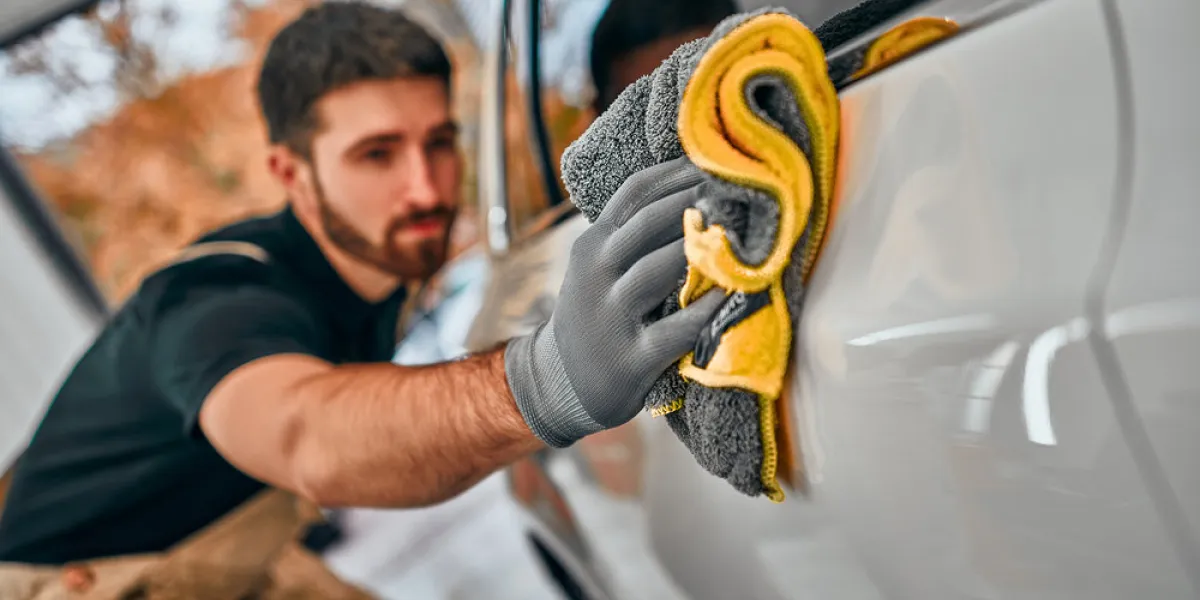 man after washing wipes white car with a rag at car wash selective focus